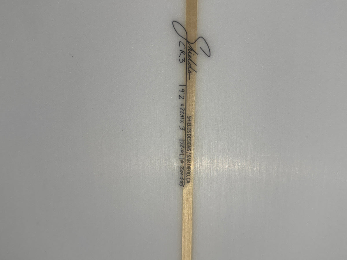 A narrow wooden stick or label with printed black text and a handwritten signature near the top, placed vertically on a plain light gray background.