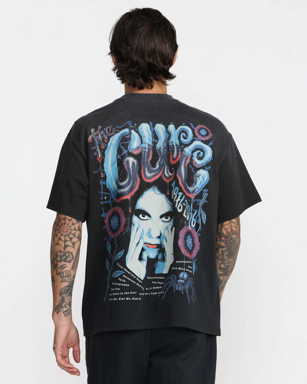 RVCA x The Cure Black T-Shirt modeled from behind, showcasing a relaxed fit and large colorful back graphic featuring Robert Smith and The Cure band lettering.