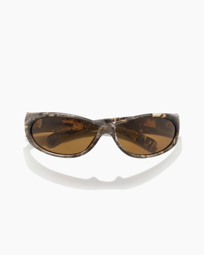 Demon Speed Camo Sunglasses featuring brown tinted lenses, a woodland camouflage frame, and a sporty wraparound design, shown from an angled front view.