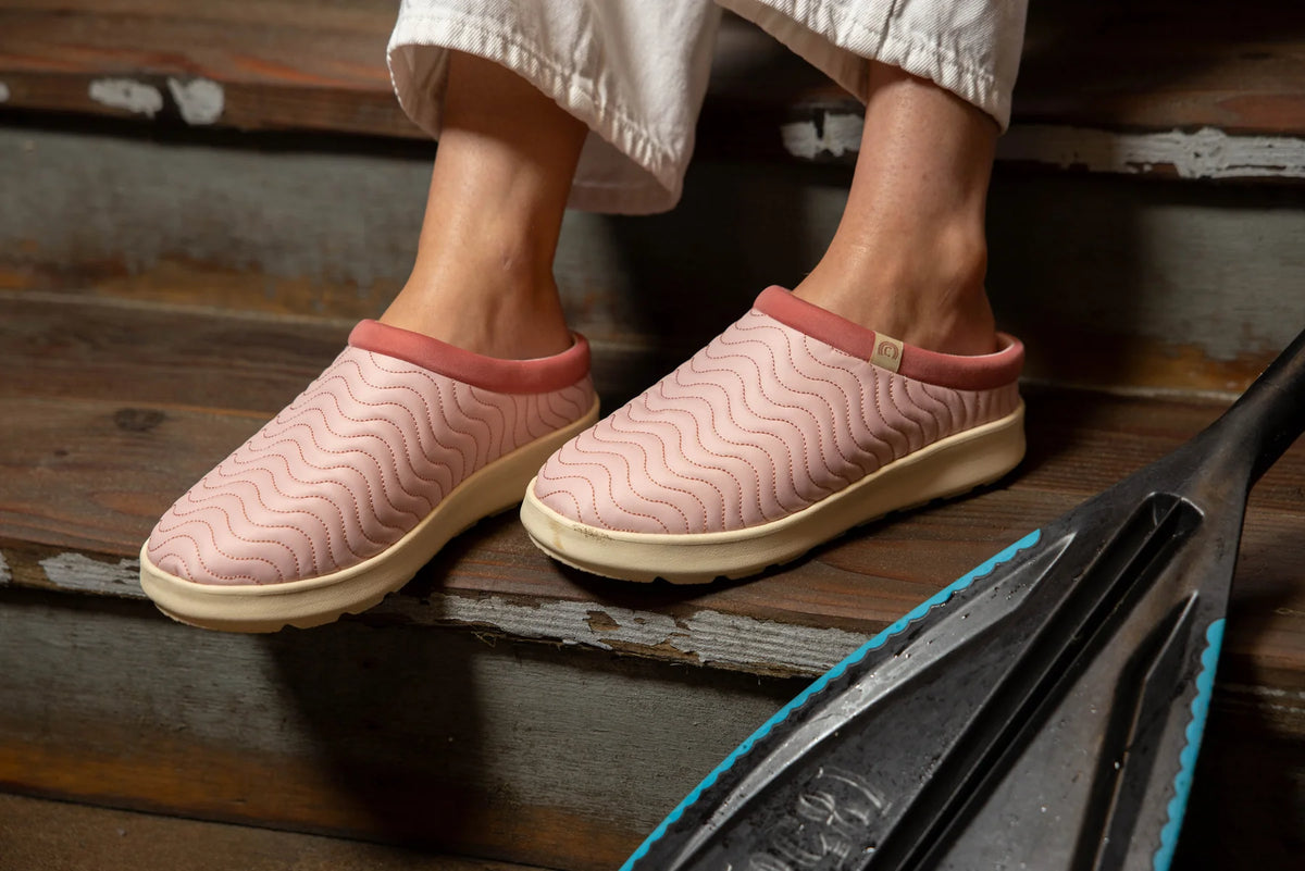 Cobian FlipSlip Mauve slip-on shoes worn on wooden steps, showcasing pink quilted wave-pattern uppers and cream-colored soles.