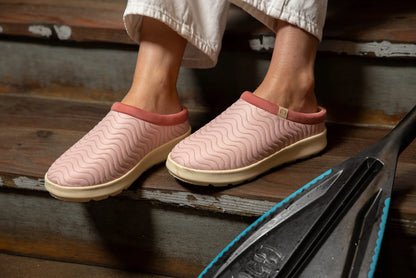 Cobian FlipSlip Mauve slip-on shoes worn on wooden steps, showcasing pink quilted wave-pattern uppers and cream-colored soles.