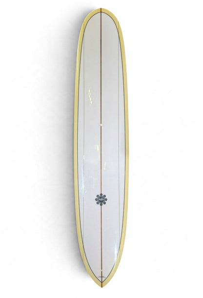 A white 9'2 Hank Byzak with tan rales with a flower emblem toward the bottom of the board. 