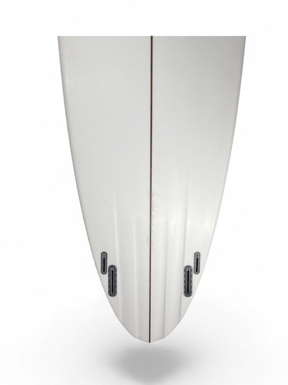 Tail of a white surfboard with 4 black fin boxes and channels. 