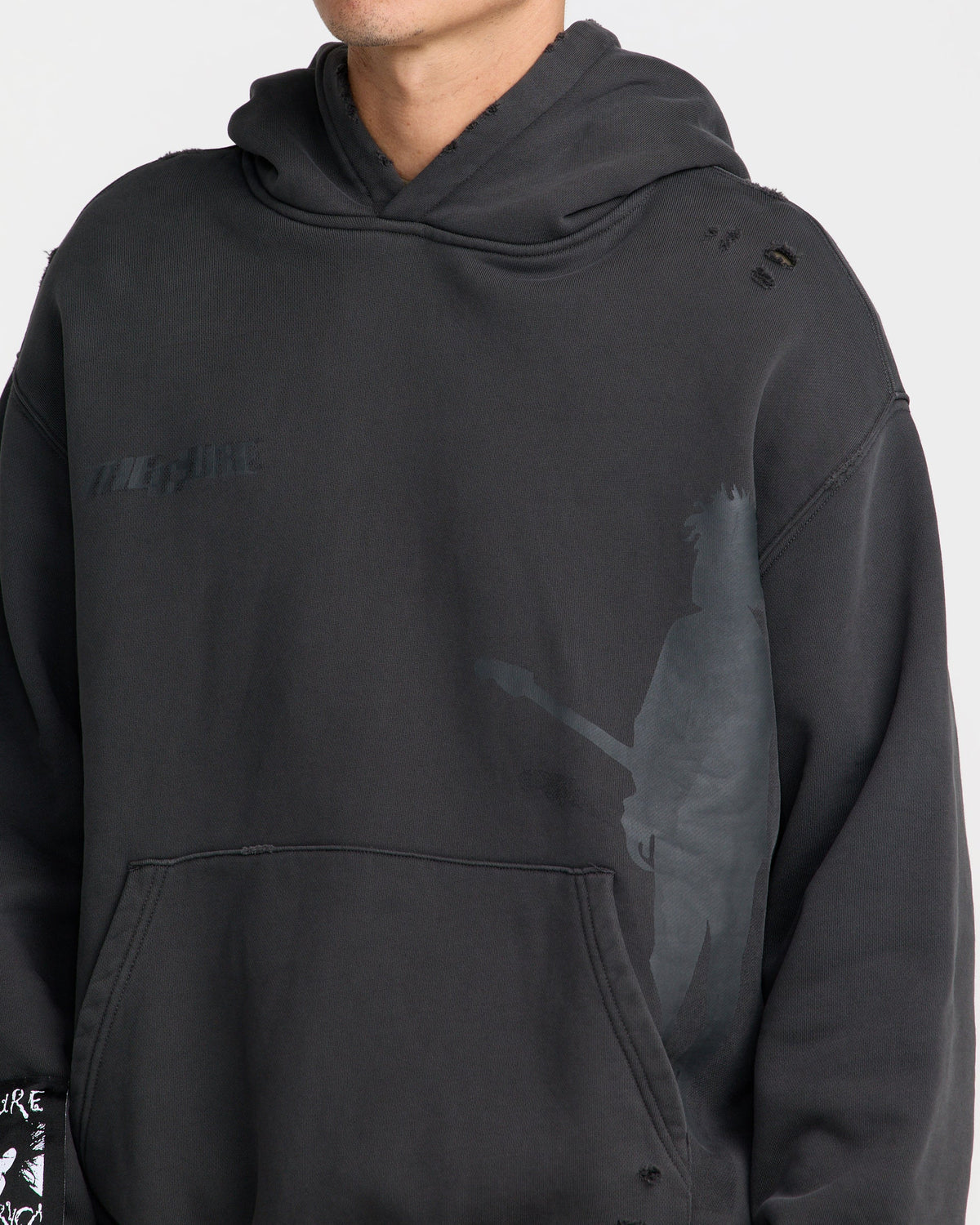 Close-up of The Cure Hoodie in washed black featuring tonal band logo, guitarist silhouette graphic, distressed shoulder details, and front kangaroo pocket.