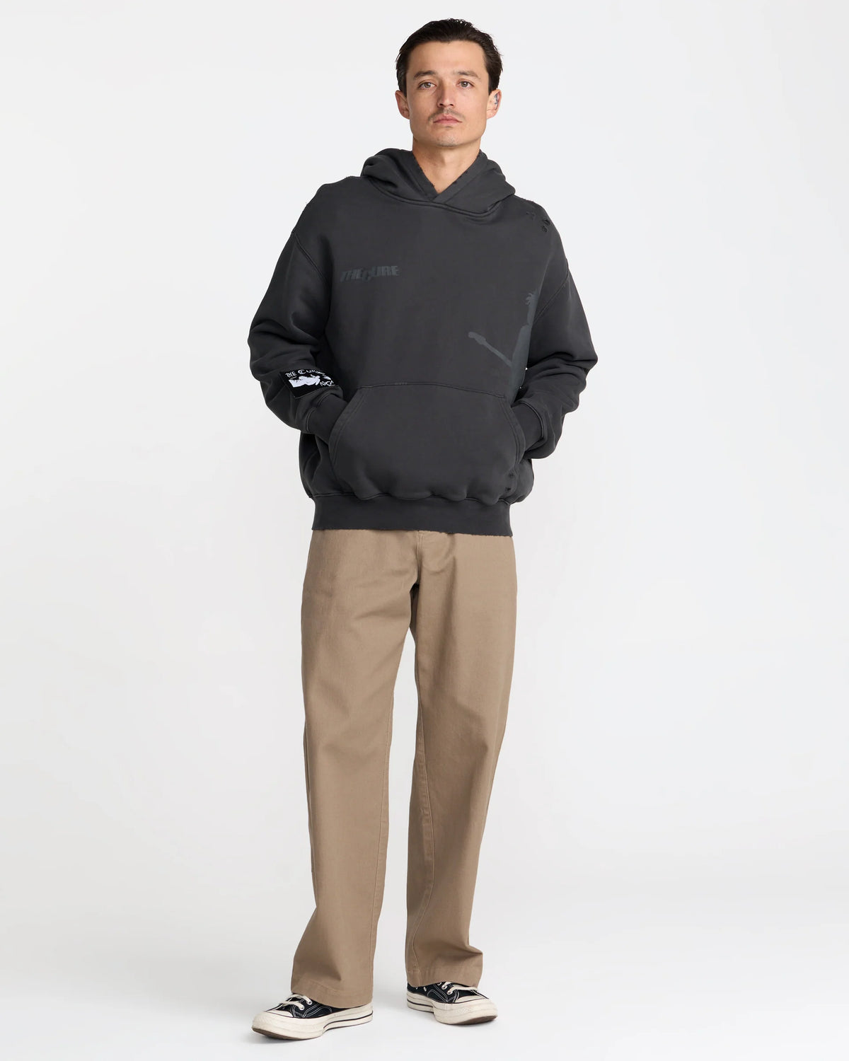 The Cure Boys Don't Cry Hoodie in washed black styled with tan pants and sneakers, showcasing the relaxed oversized fit and vintage-inspired band graphics.