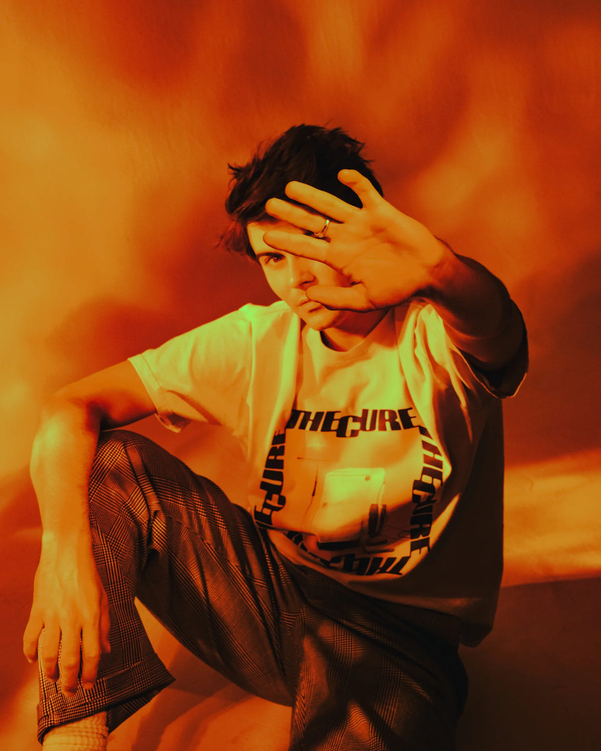 RVCA x The Cure Cream T-Shirt featuring a bold front graphic with vintage appliances and The Cure lettering, modeled under dramatic orange lighting.