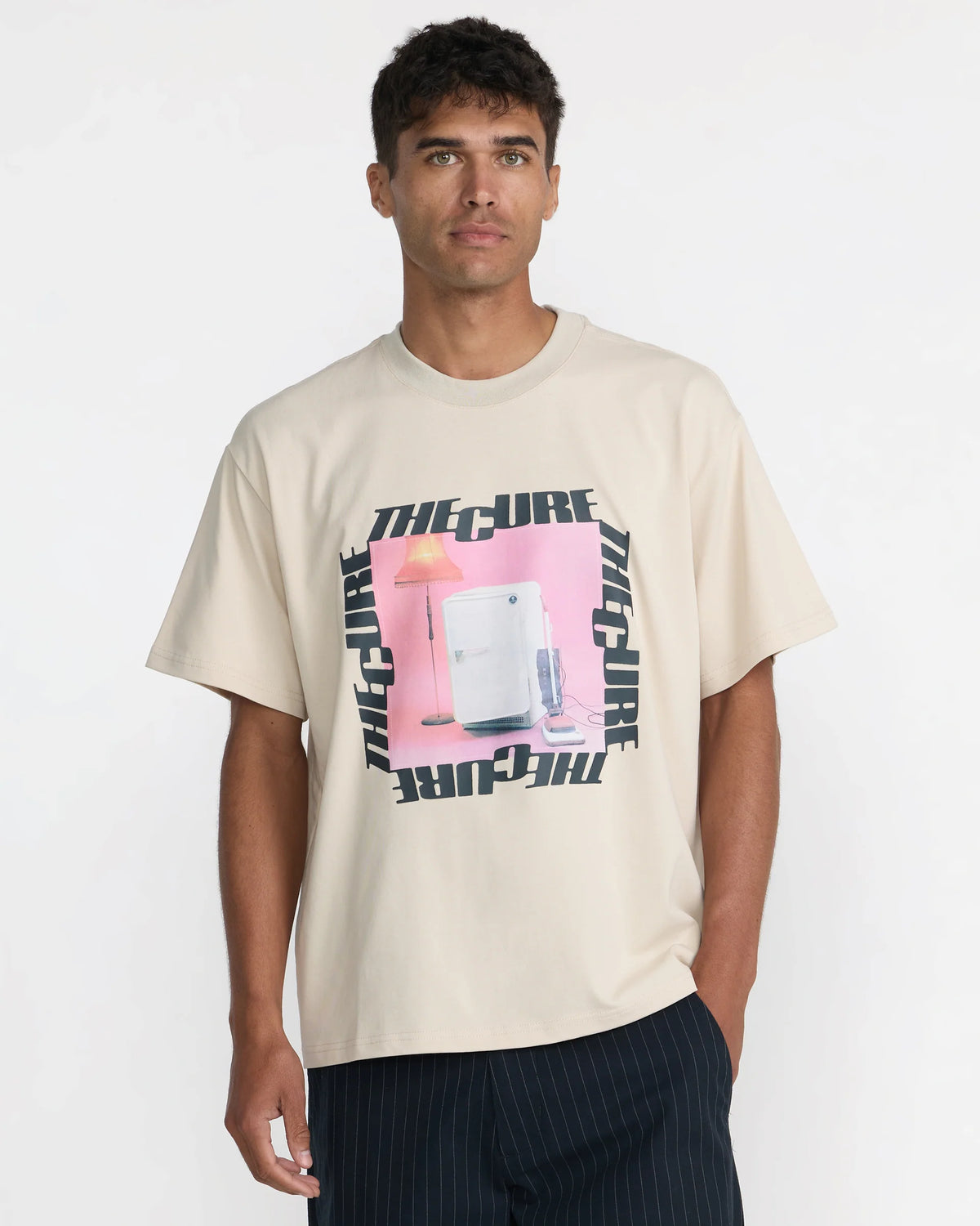RVCA x The Cure Tee in cream shown on a model, featuring a relaxed fit, crew neckline, and pink graphic framed by black The Cure logos.