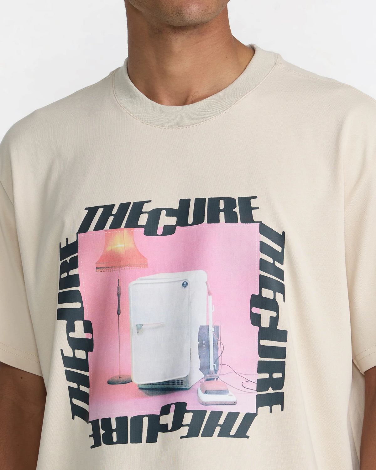 Close-up of RVCA x The Cure Tee in cream showcasing the pink refrigerator, floor lamp, and vacuum cleaner graphic surrounded by black The Cure lettering.