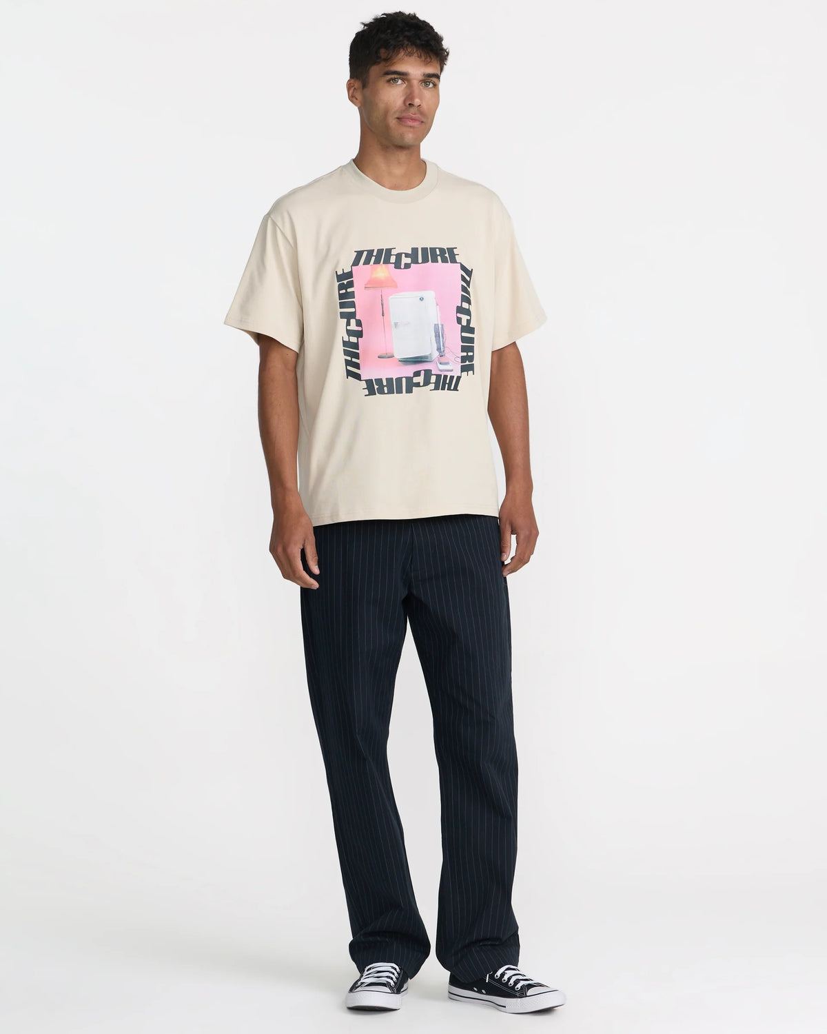 RVCA x The Cure Cream T-Shirt styled with black pinstripe pants and sneakers, showcasing the relaxed fit and bold vintage-inspired front graphic.